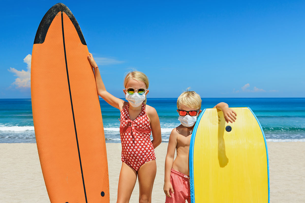 Children on beach with surf boards wearing COVID face masks